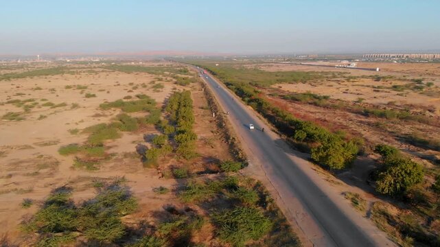 Aerial view of the Makran Coastal Range featuring a long asphalt road cutting through the arid desert landscape with sparse vegetation in Pasni, Balochistan, Pakistan.