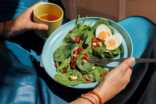 Woman eats healthy spinach salad with egg and holds yellow mug