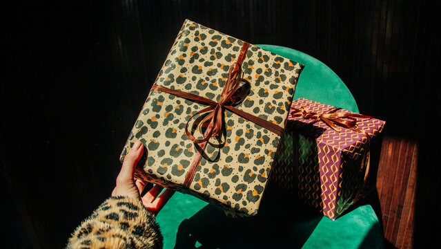 Woman holds a leopard print gift box over a green velvet armchair