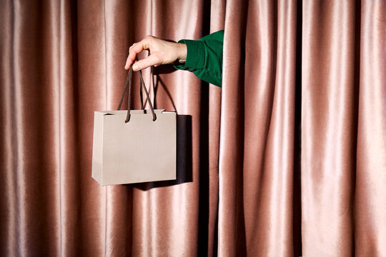 Female hand holds a gift bag through a pink velvet curtain indoors