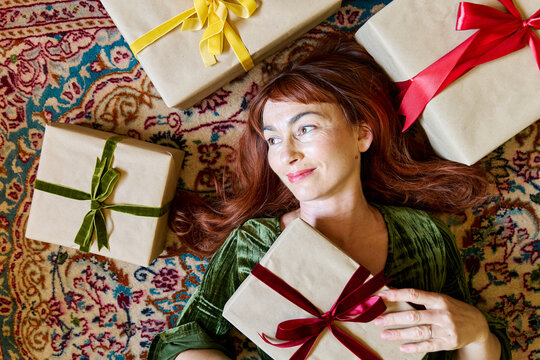 Smiling woman lying on a rug surrounded by wrapped Christmas gifts