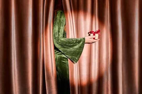 Woman in green velvet dress holding a gift behind a theater curtain