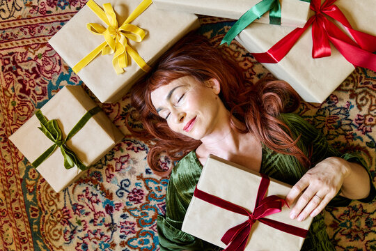 Woman lies on a rug surrounded by wrapped Christmas gifts