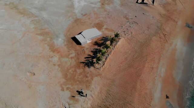 Aerial view of Makran Coastal Range beach with a small building, palm trees, and people walking on the sand in Pasni, Balochistan, Pakistan.