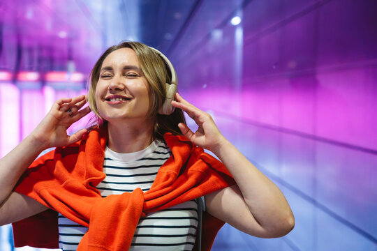 Happy woman in sweater listens to music at neon metro station