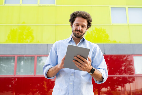 Smiling businessman uses a digital tablet outdoors by a colored wall
