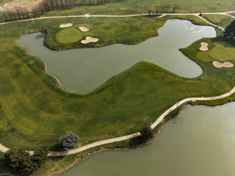 Aerial view of a golf course featuring green fairways, sand bunkers, and water hazards in Opera, Lombardy, Italy.