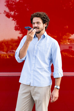 Businessman records a voice message on smartphone by red wall