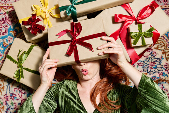 Woman in green dress holds Christmas gift over face on Persian rug