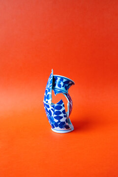 A broken blue porcelain vase stands on a red background