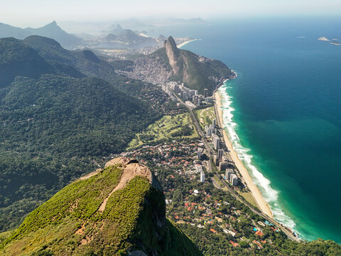 Aerial view of the coastline of Rio de Janeiro featuring the Dois Irmaos peaks, lush mountains, urban high-rise buildings, and sandy beaches in Rio de Janeiro, Rio de Janeiro, Brazil.
