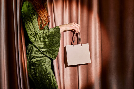 Woman in green velvet dress holds a gift bag by a theater curtain