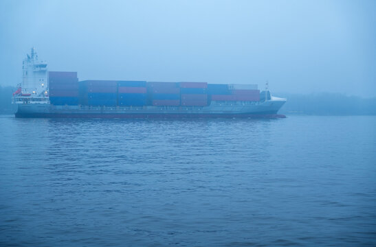 View of a large container ship loaded with colorful shipping containers sailing through the misty waters of the port in Klaipeda, Klaipeda County, Lithuania.