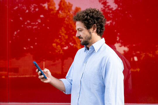 A businessman uses a smartphone against a red wall