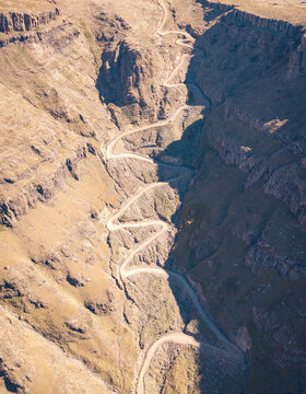 Aerial view of the winding dirt road of Sani Pass snaking through the dramatic rocky cliffs and steep mountain terrain of Sani Pass, Lesotho, Lesotho.