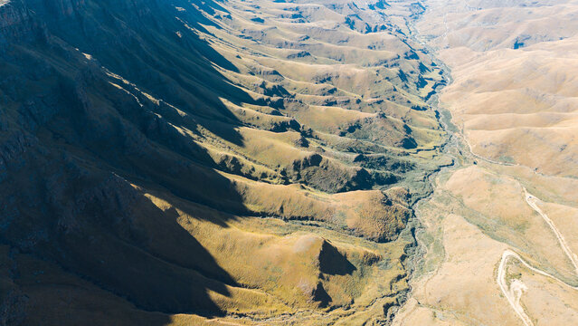 Aerial view of the winding mountain road of Sani Pass with dramatic shadows cast across the rugged slopes of the Drakensberg mountains in Sani Pass, Lesotho, Lesotho.