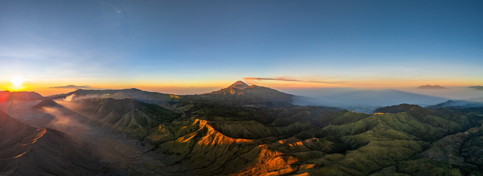 Aerial view of Bukit Keciri in the volcanic landscape of Mount Bromo at sunrise with golden light illuminating the ridges and valleys in Kecamatan Tosari, Jawa Timur, Indonesia.