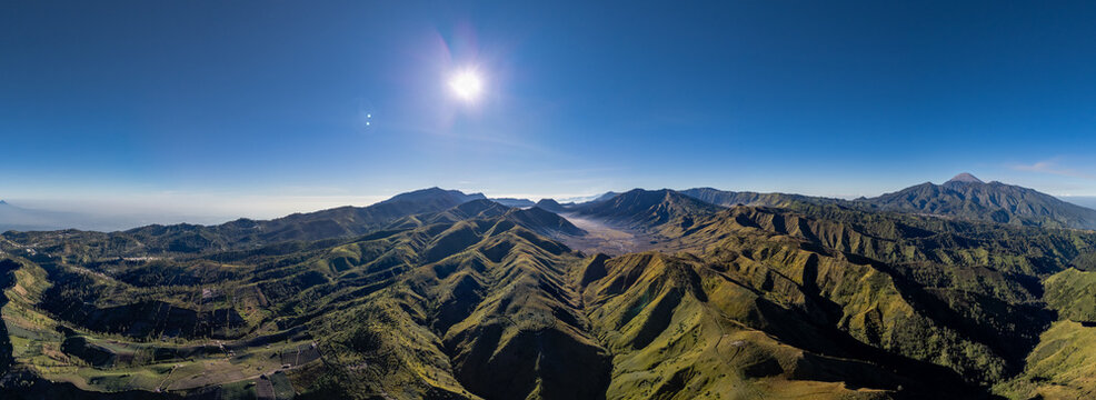 Aerial view of Bukit Keciri in the mountainous landscape of East Java, featuring lush green ridges and valleys under a clear blue sky in Kecamatan Tosari, Jawa Timur, Indonesia.