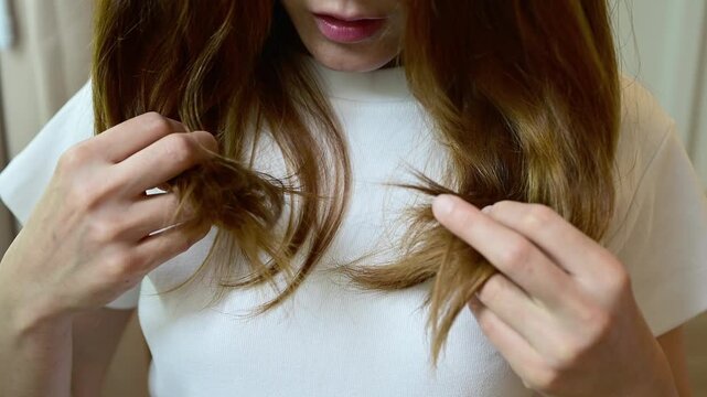Asian woman holding and checking her damaged split ended hair. Hair damage is risk for further damage and breakage. It may also look dull or frizzy and be difficult to manage.