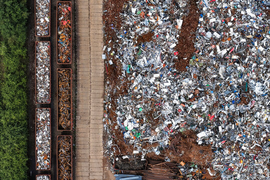 Aerial view of a scrap metal yard featuring train cars filled with metal waste and large piles of shredded scrap metal next to a concrete path in Unterwellenborn, Thuringia, Germany.