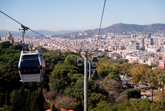 Aerial view of the Teleferic de Montjuic cable car gliding over lush green trees with the sprawling cityscape of Barcelona in the background. Barcelona, Catalonia, Spain.