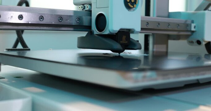 Close-up of a 3d printer nozzle printing a plastic object on the build plate in a modern workshop, with soft blue tones and machinery details