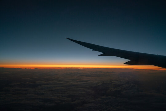 View of an airplane wing silhouetted against a vibrant sunset sky above a thick layer of clouds, New York, New York, United States.