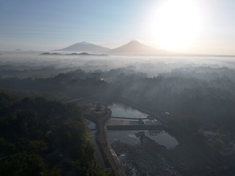 Aerial view of a misty river landscape with Mount Merapi in the background during sunrise in Yogyakarta, Special Region of Yogyakarta, Indonesia.