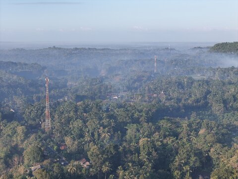 Aerial view of communication towers rising above the dense tropical forest and lush vegetation in the misty landscape of Yogyakarta, Special Region of Yogyakarta, Indonesia.