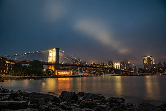 Aerial view of the illuminated Brooklyn Bridge spanning the East River with the New York City skyline in the background under a dark night sky, New York, New York, United States.