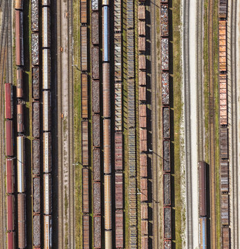 Aerial view of a busy railway yard in Saalfeld with numerous freight trains and cargo carriages lined up on parallel tracks under bright sunlight. Saalfeld, Thuringia, Germany.