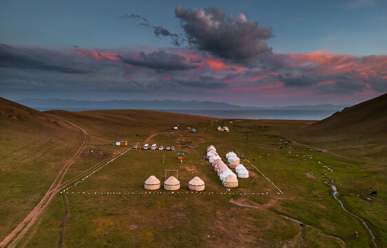 Aerial view of a traditional yurt camp situated on the grassy plains near Song-Kul lake under a dramatic sunset sky in Naryn Region, Kyrgyzstan.