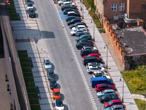 Aerial view of a street lined with numerous parked cars alongside a historic brick building and paved walkways in Gdansk, Pomeranian Voivodeship, Poland.