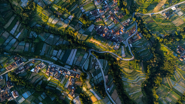 Aerial view of terraced agricultural fields and small village houses nestled along winding roads in the golden hour light in Selo, Central Java, Indonesia.