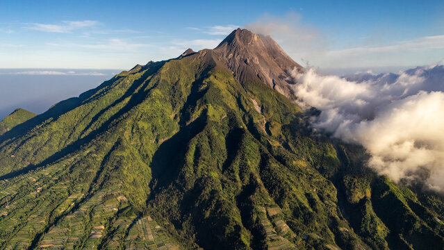 Aerial view of Mount Merapi with lush green slopes, volcanic peak, and agricultural fields at the base in Selo, Central Java, Indonesia.