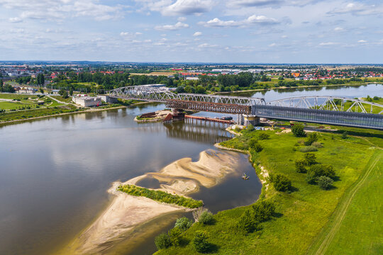 Aerial view of the historic Tczew bridge spanning the Vistula river, surrounded by lush green riverbanks and sandy shoals under a bright summer sky in Tczew, Pomeranian Voivodeship, Poland.
