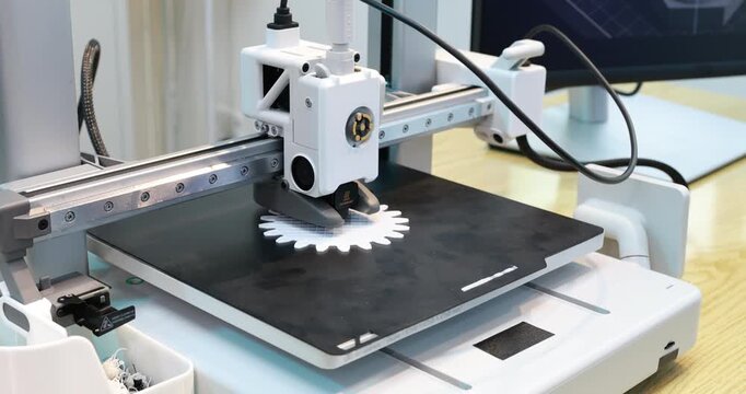 Desktop 3d printer printing a white gear on a build plate in a modern workspace