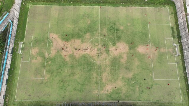 Aerial view of Jakarta International Stadium with players on the soccer field showing grass patches and white markings in Tanjung Priok, Jakarta, Indonesia.