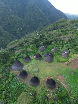 Aerial view of Waerebo Village featuring traditional cone-shaped houses with thatched roofs nestled in a lush green mountain valley in Satar Mese Barat, East Nusa Tenggara, Indonesia.