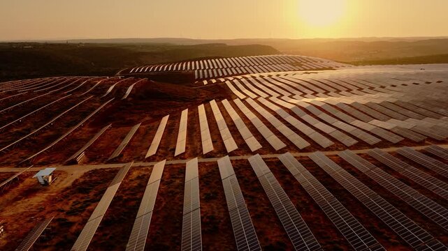 Aerial view of expansive photovoltaic arrays arranged across rolling countryside in warm evening light. 