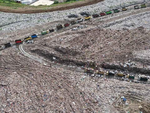 Aerial view of TPA Suwung landfill with numerous trucks transporting waste along dirt roads in Kecamatan Denpasar Selatan, Bali, Indonesia.