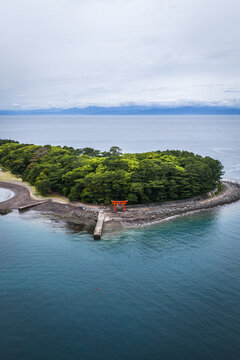 Aerial view of the iconic red torii gate at Mihama Beach surrounded by lush green trees and rocky coastline in Numazu, Shizuoka, Japan.