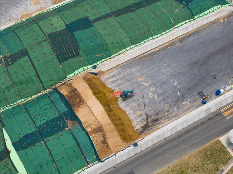 Aerial view of the Moor Bio Energy biomass facility with large piles of organic material covered by green netting and a tractor working on site in Grantham, England, United Kingdom.