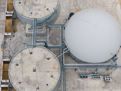 Aerial view of the Moor Bio Energy biomass facility featuring large industrial storage tanks and a dome-shaped digester with connecting pipes in Grantham, England, United Kingdom.