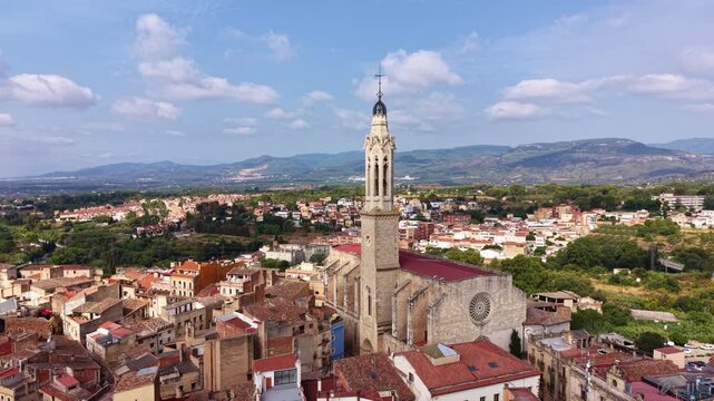 Aerial view of Valls city center in Catalonia, Spain, featuring the Gothic bell tower and rose window facade of the church surrounded by terracotta rooftops and mountains
