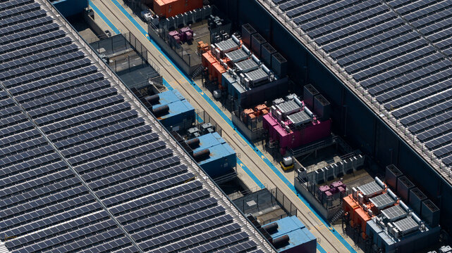 Aerial view of a large industrial data center facility featuring extensive rooftop solar panel arrays and rows of industrial cooling units in Hemel Hempstead, England, United Kingdom.