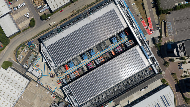 Aerial view of a large industrial facility featuring extensive rooftop solar panels, HVAC units, and surrounding parking areas in Hemel Hempstead, England, United Kingdom.