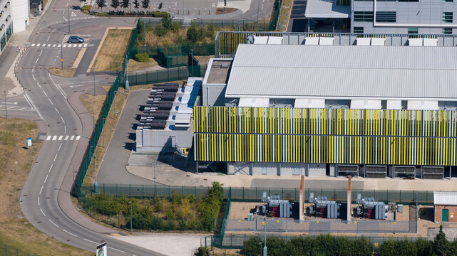 Aerial view of the Kao Data campus with modern industrial architecture, yellow and green vertical louvers, surrounding roads, and electrical infrastructure in Harlow, England, United Kingdom.