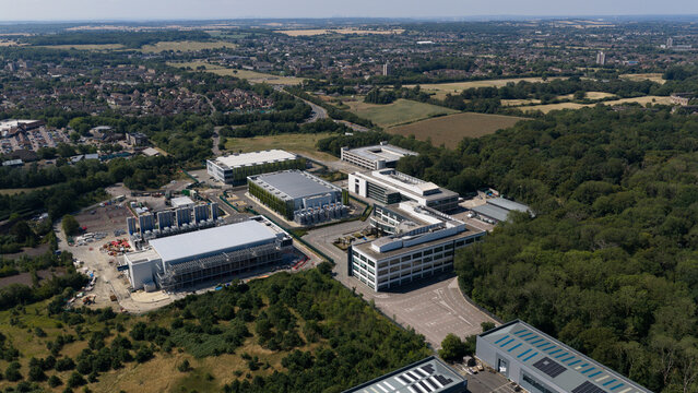 Aerial view of the Kao Data campus featuring modern industrial buildings and data center facilities surrounded by lush green woodland in Harlow, England, United Kingdom.