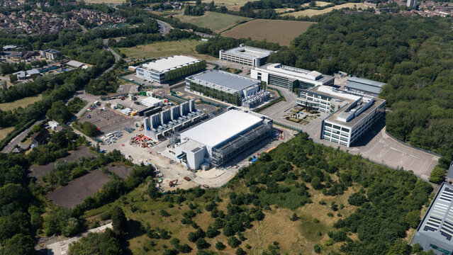 Aerial view of the Kao Data campus featuring modern industrial buildings, data center facilities, surrounding woodland, and parking areas in Harlow, England, United Kingdom.